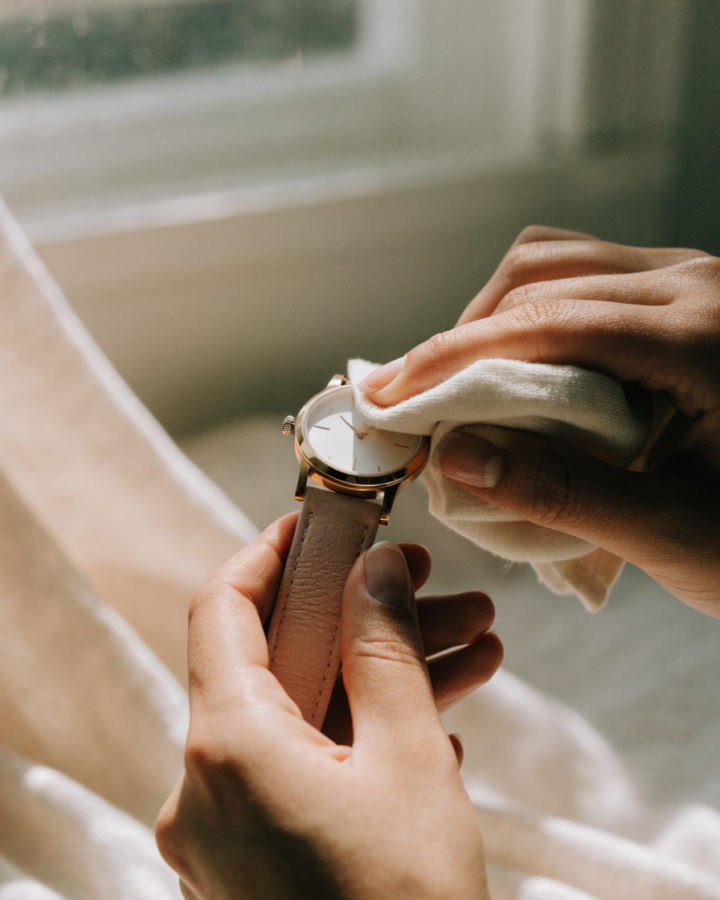 Mãos limpando com flanela um relógio feminino de caixa dourada e pulseira rosé